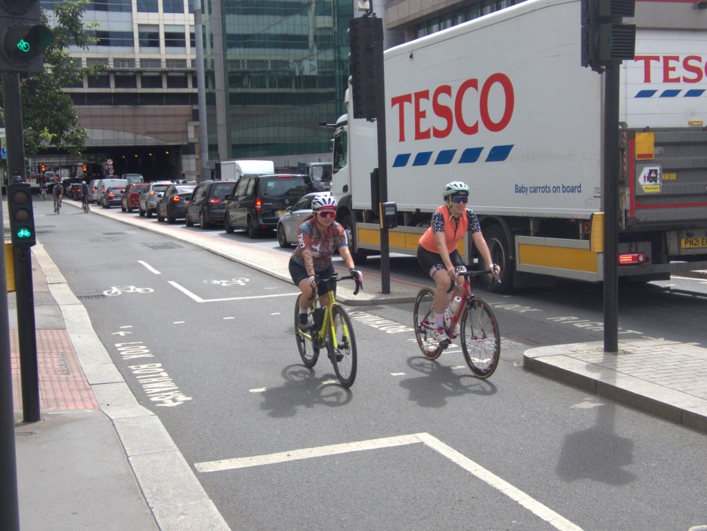 Two people riding west on Cycleway 3 in London, on the north side of Southwark Bridge
