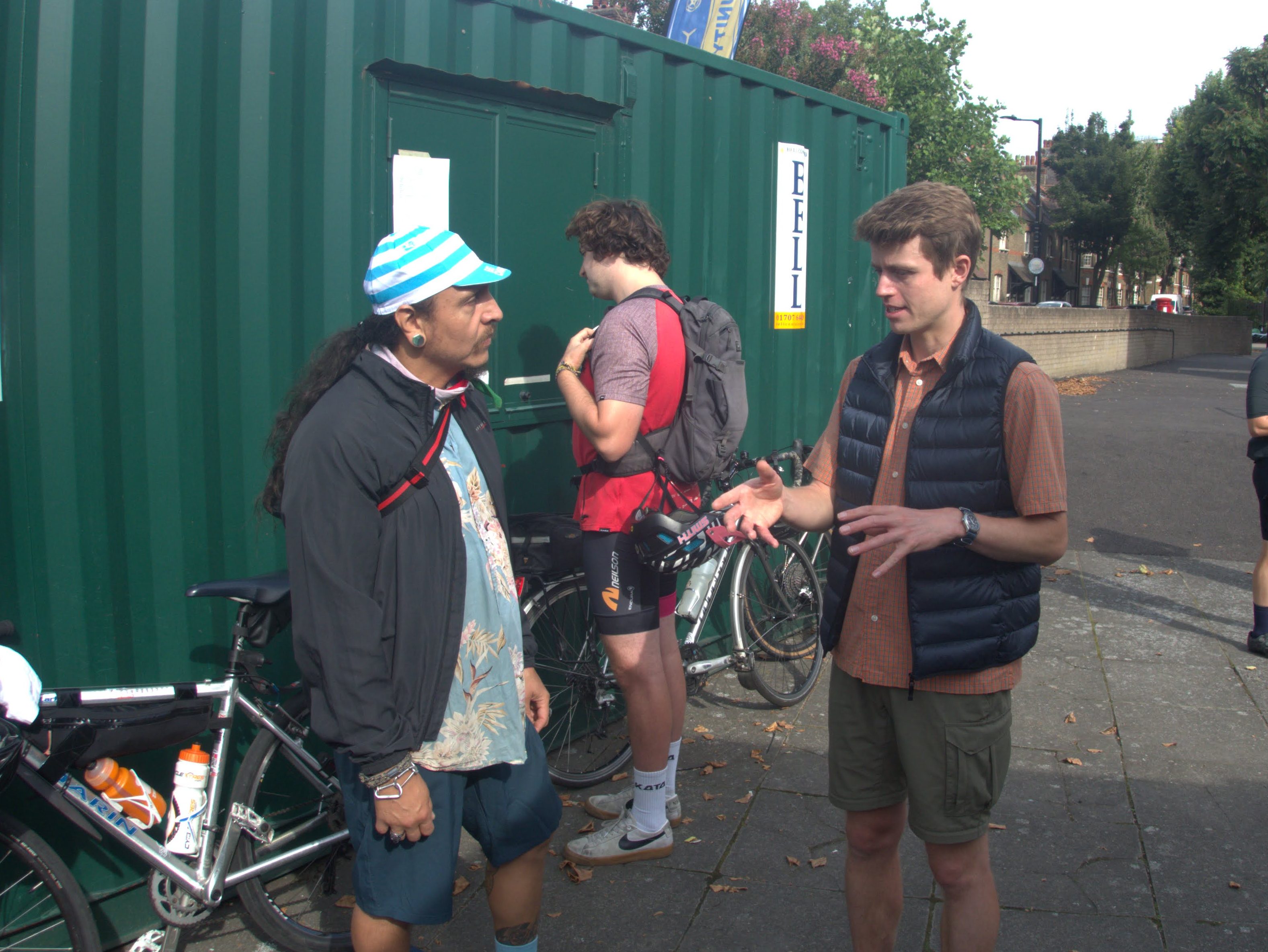 Two people facing each other and conversing. bicycles are in the background.