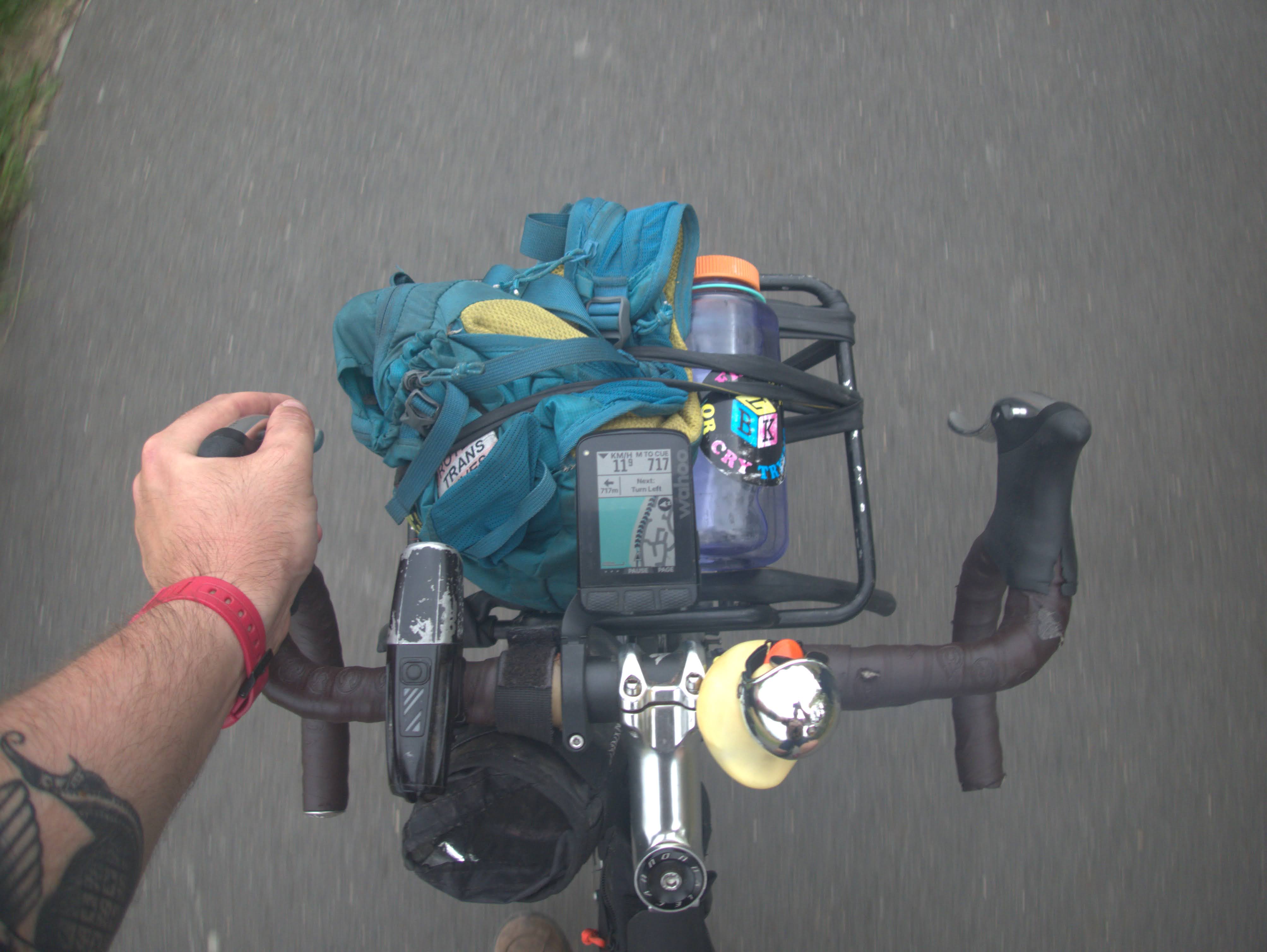 A 'point of view' shot of my bicycle's handlebars when riding. It shows my bike's front light, the luggage rack with a small bag and a water bottle, my navigational computer, and a squeaky rubber duck.